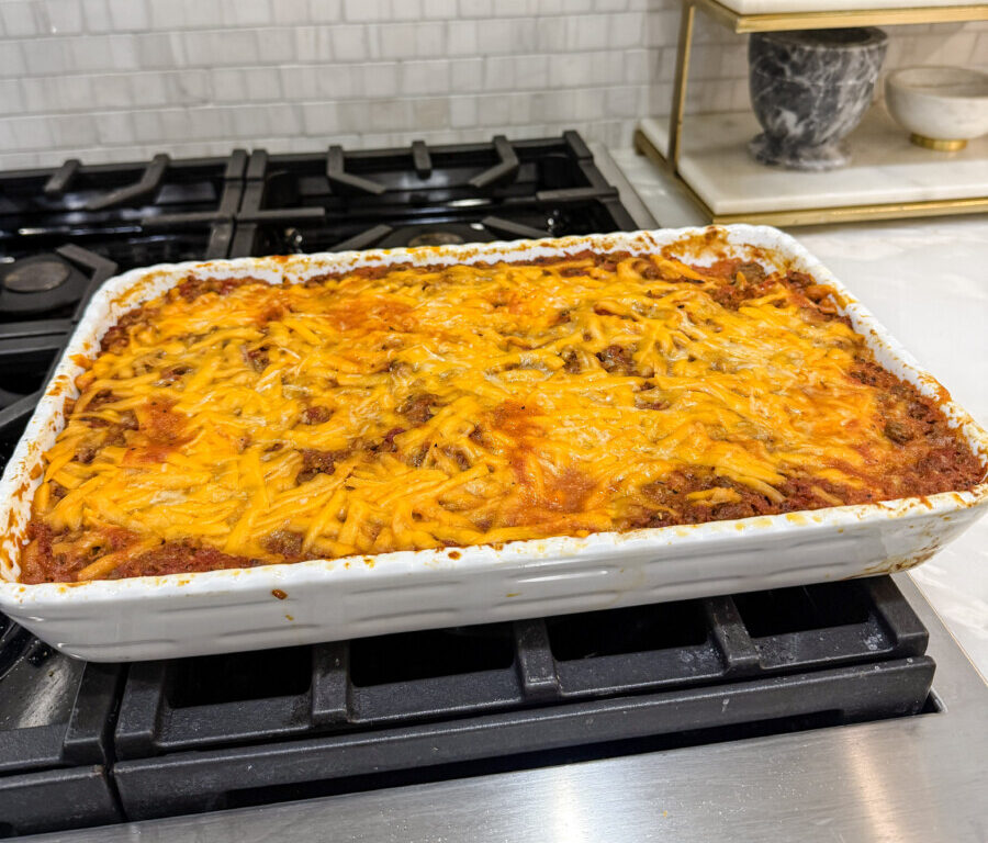 Cheesy beef noodle casserole, also known as "Husband's Delight," in a white casserole dish on a stovetop