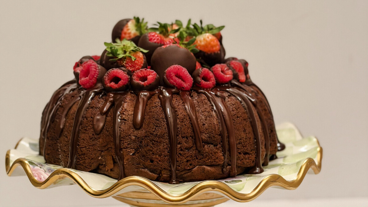 Family Savvy's Quadruple Chocolate Bundt Cake with Chocolate Ganache & fruit on top sitting on a floral ruffled cake plate