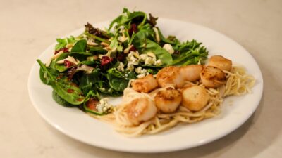 Golden pan-seared scallops with lemon butter sauce over angel hair pasta with a side of a leafy green salad