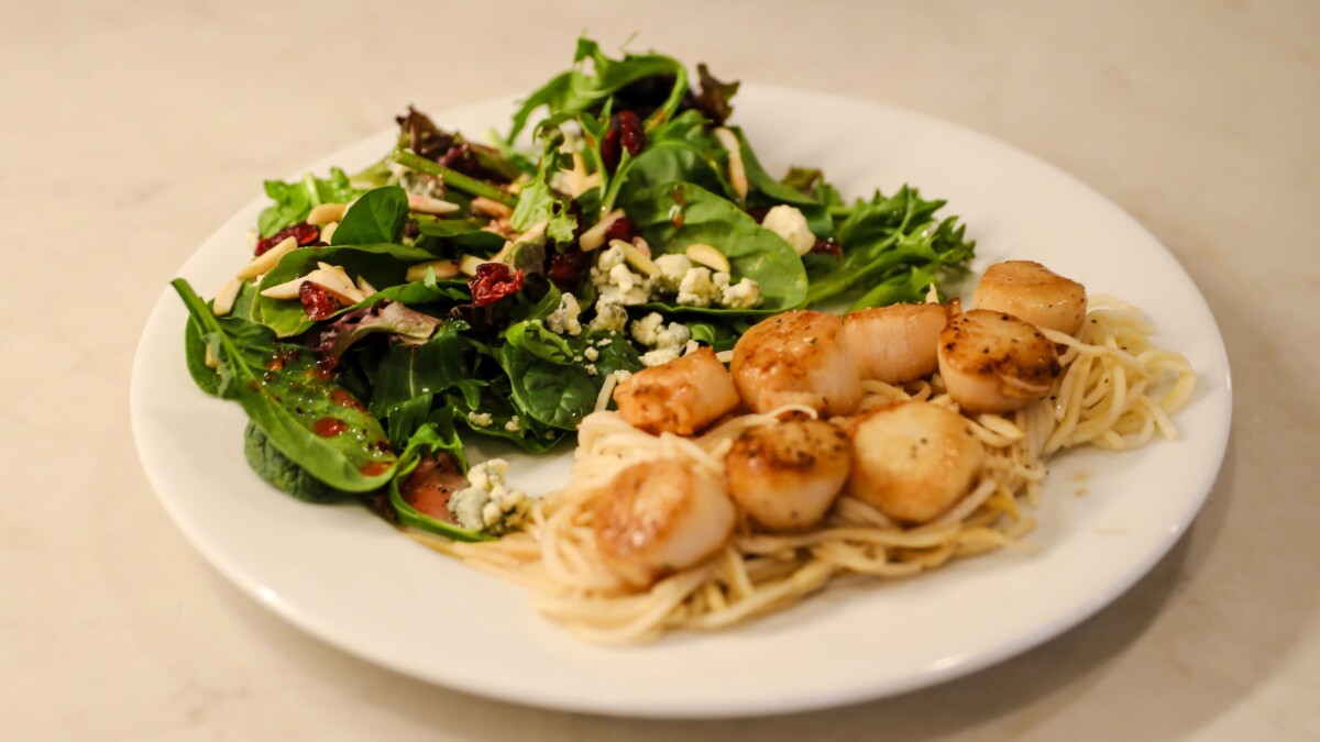 Golden pan-seared scallops with lemon butter sauce over angel hair pasta with a side of a leafy green salad