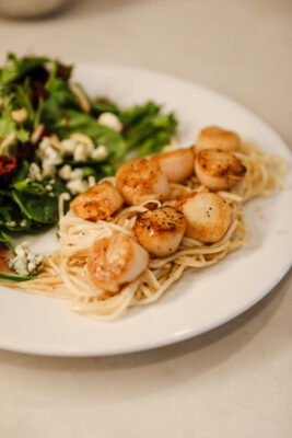 Close-up of golden pan-seared scallops with a lemon butter sauce served over angel hair pasta 