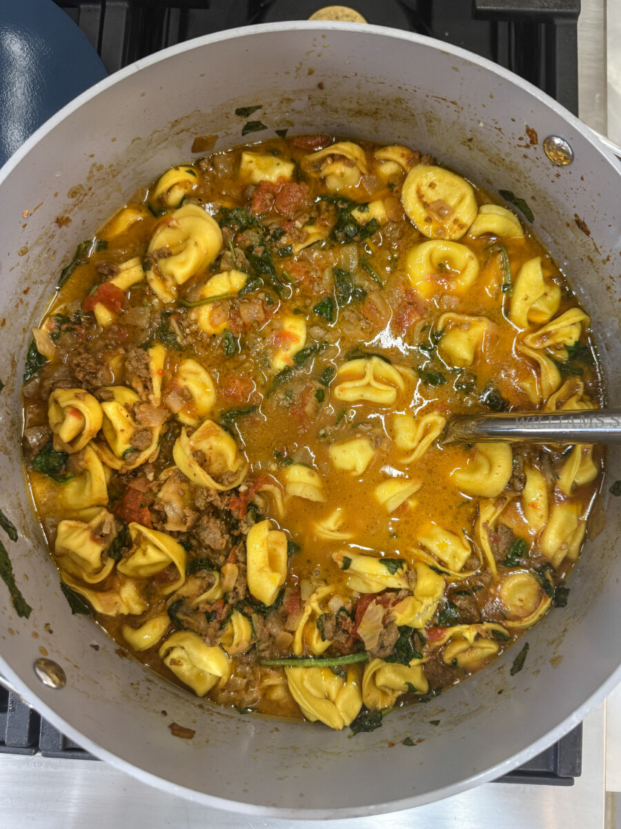 Overhead view of Family Savvy's Italian Sausage Tortellini Soup in a pot on the stovetop