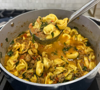 A pot full of Family Savvy's Italian Sausage Tortellini Soup with a ladle scooping some out of the pot