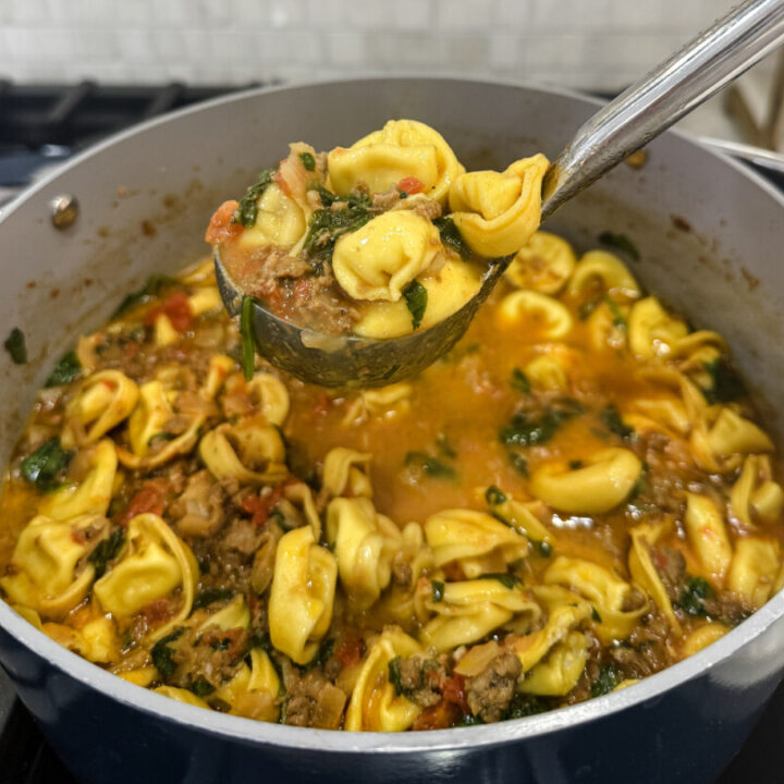 A pot full of Family Savvy's Italian Sausage Tortellini Soup with a ladle scooping some out of the pot