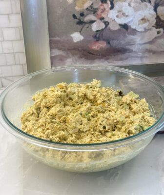 A glass bowl of Curried Chicken Salad sitting on a marble countertop
