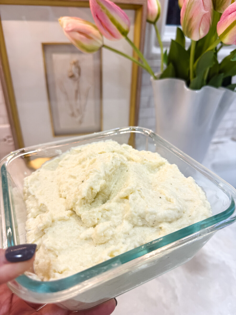 Glass bowl of Boursin Mashed Cauliflower next to pink tulips and gold and white artwork on a marble kitchen counter