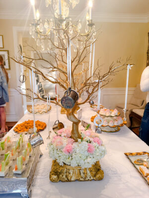 Baby shower decor on a table with a gold tree with silver baby items hanging from it