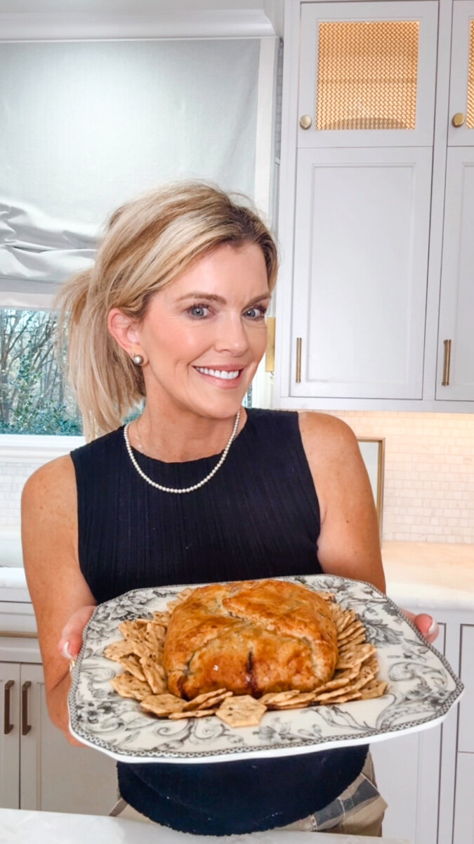Jamie Tarence of Family Savvy standing in her kitchen holding a plate of the baked brie with blackberry jam wrapped in puff pastry