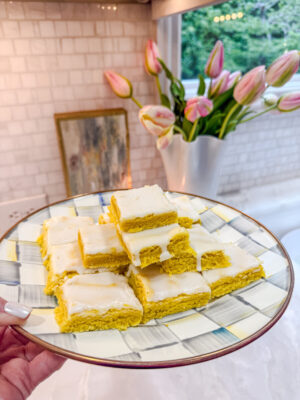 Bright yellow lemon brownies topped with a white lemon glaze on a blue and white checkered plate
