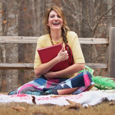 Amy Grimes of Story Paintings sitting on a blanket outside with a red book