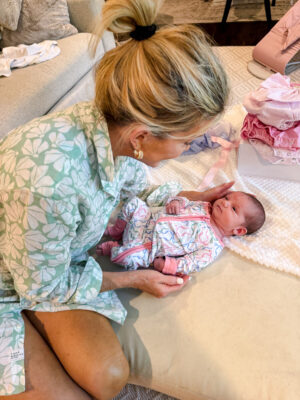 Jamie holding her newborn grandbaby Anne Parker while sitting on an ottoman, a sweet reminder of the essential baby items for grandparents to keep at home.