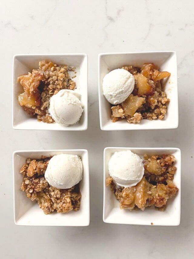 Four square white bowls filled with warm apple crisp topped with scoops of vanilla ice cream, a cozy apple cinnamon recipe perfect for dessert