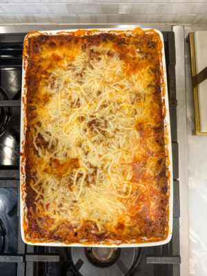 Overhead view of a cheesy baked spaghetti pie in a white casserole dish sitting on a stovetop