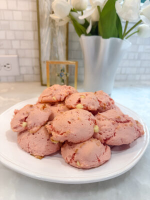 Side view of a pile of Family Savvy's strawberry white chocolate chip cookies on a white plate sitting on a marble countertop