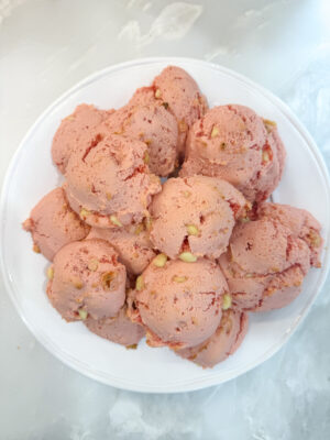 Overhead shot of a pile of Family Savvy's strawberry white chocolate chip cookies on a white plate sititng on a marble counter