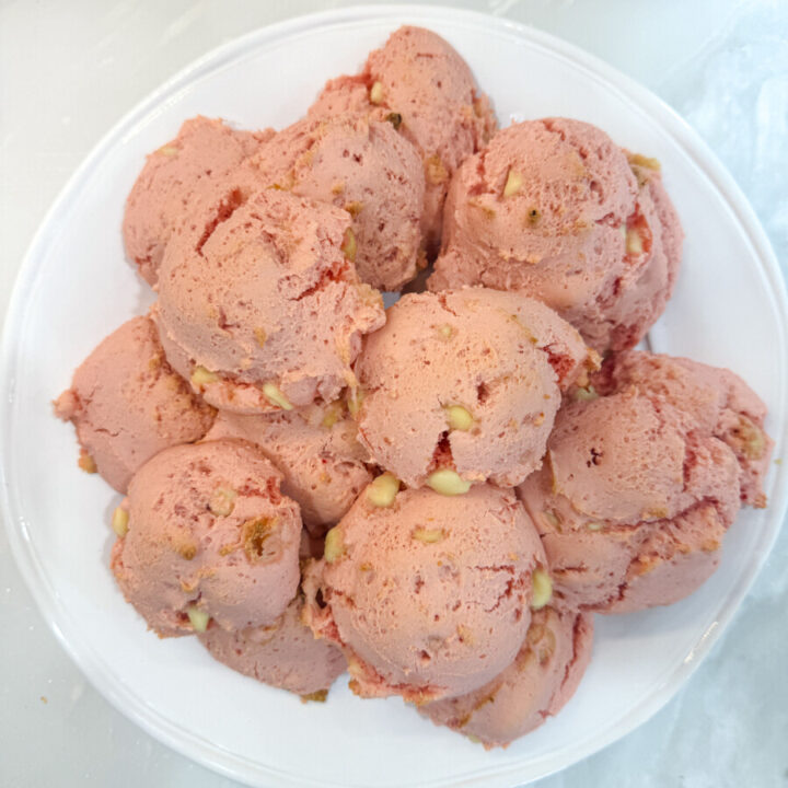 Overhead shot of a pile of Family Savvy's strawberry white chocolate chip cookies on a white plate sititng on a marble counter