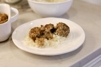 Swedish meatballs with a mushroom sauce served over white rice on a white plate on a kitchen counter