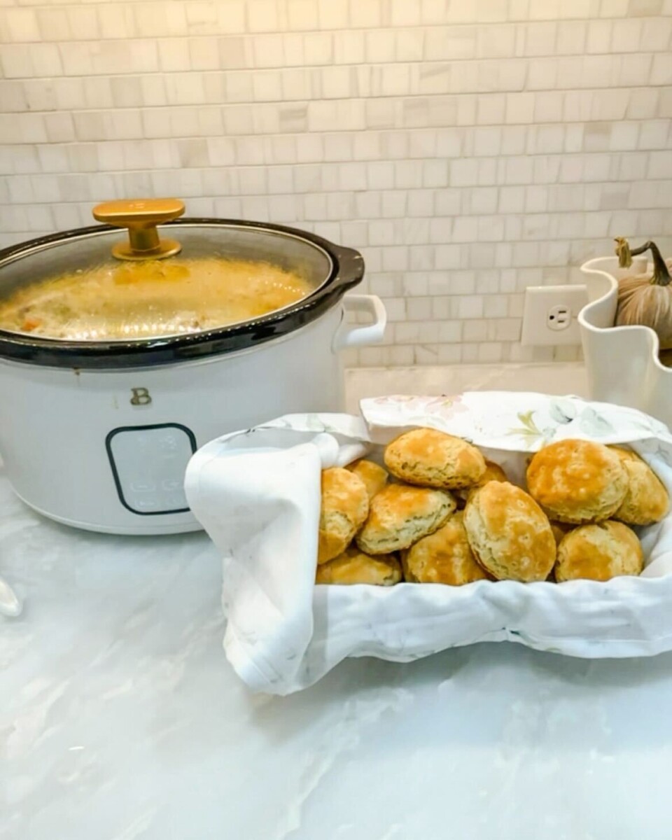 A slow cooker full of Crockpot Chicken Pot Pie is on a marble countertop next to a basket of golden biscuits