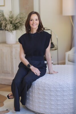 Dana Wolter of Dana Wolter Interiors sitting on an ottoman in a light and bright living room
