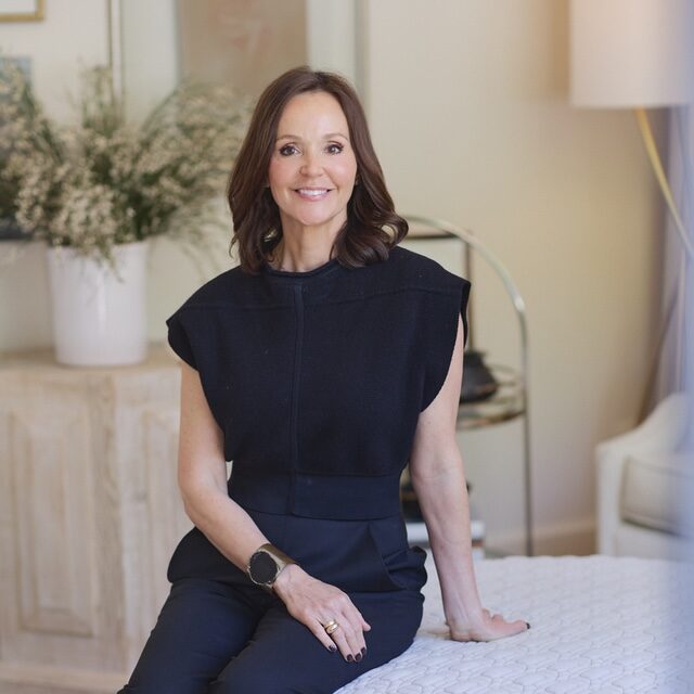 Dana Wolter of Dana Wolter Interiors sitting on an ottoman in a light and bright living room