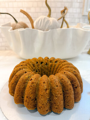 Close-up of Family Savvy's unfrosted pumpkin carrot Bundt cake on a white marble kitchen countertop with velvet pumpkins behind it