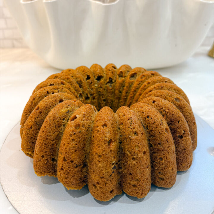 Close-up of Family Savvy's unfrosted pumpkin carrot Bundt cake on a white marble kitchen countertop with velvet pumpkins behind it