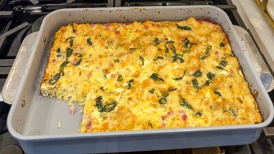 Family Savvy's Overnight Mexican Breakfast Casserole in a casserole dish on the stovetop with a piece of the casserole cut out of the dish