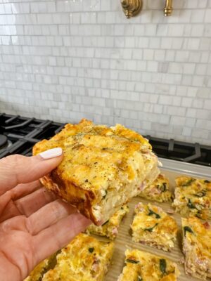 Close-up of a hand holding a square piece of the overnight Mexican Breakfast Casserole