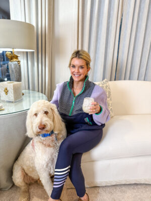 Jamie Tarence of Family Savvy sitting on her white couch in her living room with her goldendoodle Tucker sitting on the floor next to her