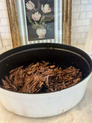 A Dutch oven full of cooked shredded rump roast sitting on the kitchen counter