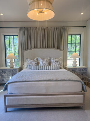 Close-up of Jamie's master bedroom at her lake home. The bed is made with an ivory coverlet along with a variety of a misty blue-green pillows and blankets.