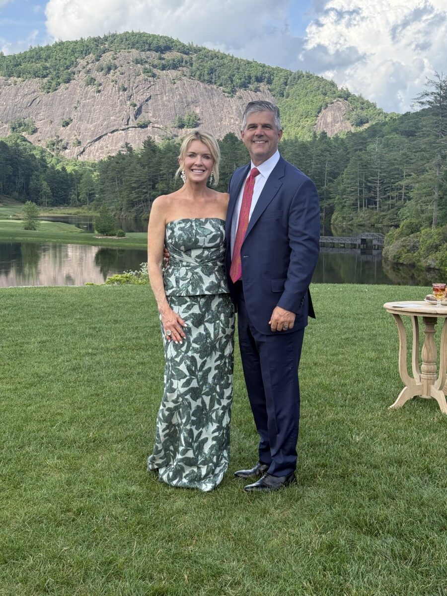 Jamie and Zane standing outside surrounded by the mountains. Jamie wearing a green dress and Zane wearing a suit with a red tie.