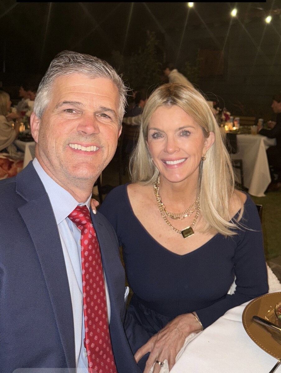 Jamie sitting at a table with Zane. Jamie is wearing a black dress, and Zane is wearing a suit with a red tie.